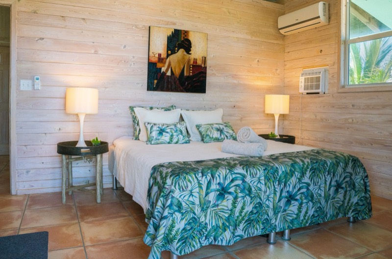 Guest bedroom with palm-print linens and lit lamps against a pale timber wall