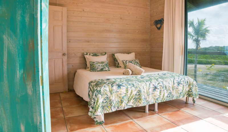 Bedroom four framed by a distressed turquoise door, glass door to a palm outside