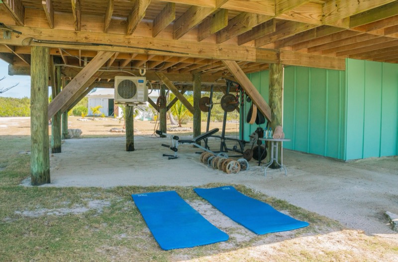 The island gym under the house: yoga mats on sand, weight rack behind