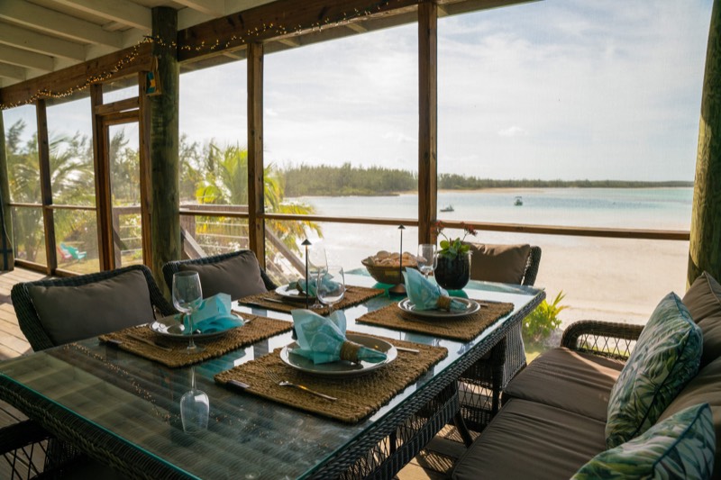 Screened porch dining table set for four, looking straight out over white sand and the bay